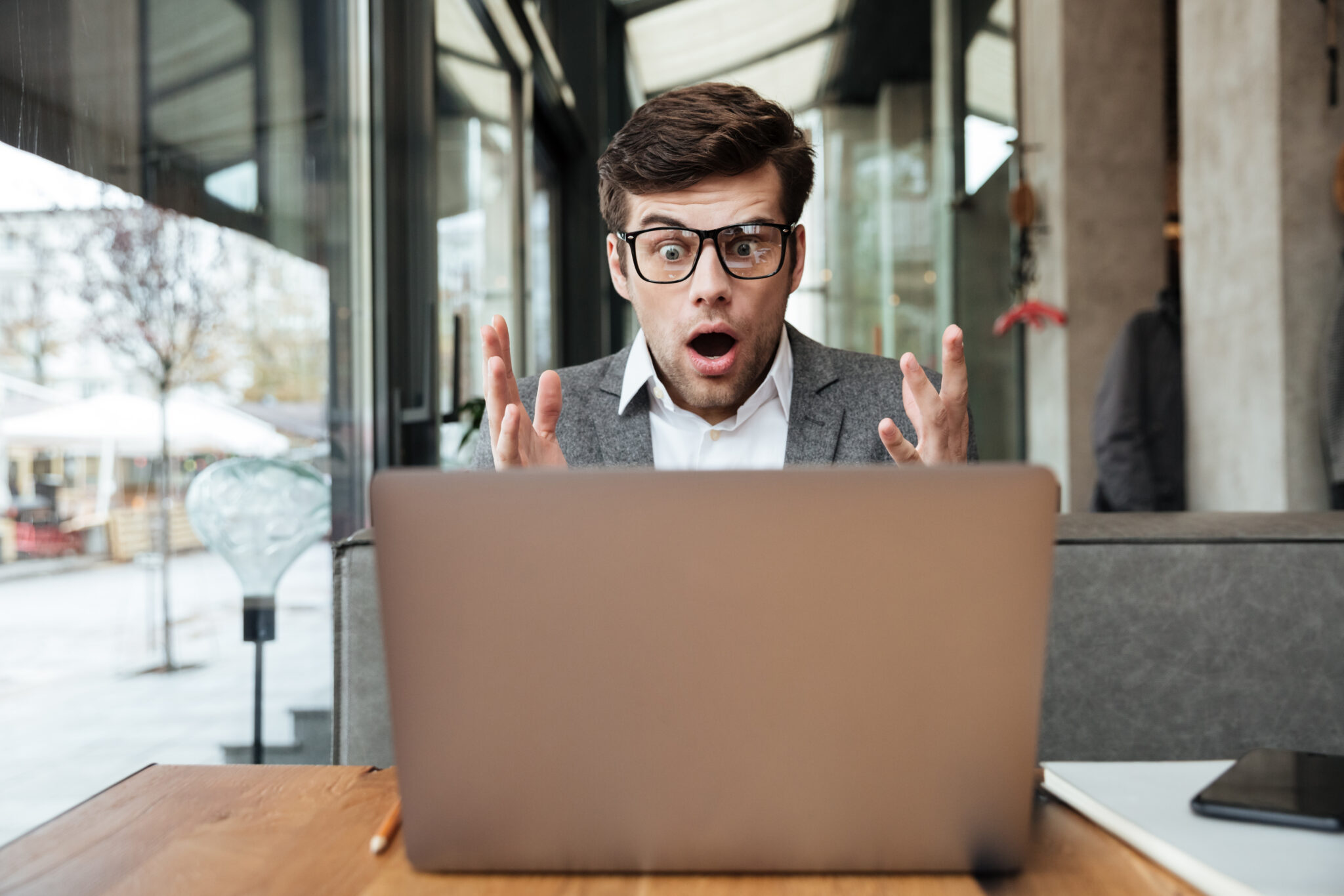 shocked business man in eyeglasses sitting by table in cafe